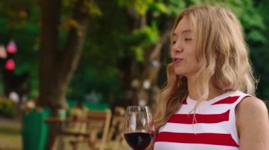 Dalgalı sarı saçlı, çok çekici beyaz bir kadının yakından çekilmiş bir fotoğrafı. Elinde şarap kadehi var ve dışarıda bir kafede kıkırdıyor. ARRI Alexa Mini 'de çekilen.