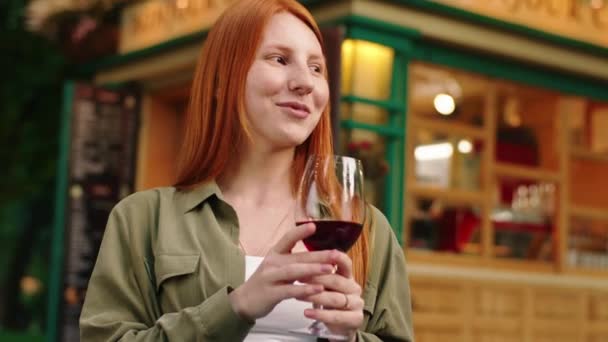 Blisko ujęcia rudej młodej kobiety, w zielonej bluzce z białą bluzką, pije wino podczas rozmowy i śmieje się na zewnątrz w parku. — Wideo stockowe
