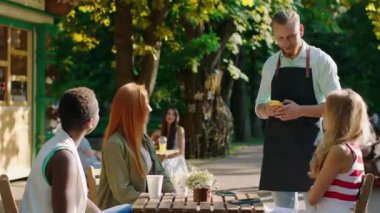 Parkın ortasında, kafeden karizmatik bir barista adam siparişi alıyor. Büyük gülümsemeli, çok kültürlü bir grup kadın.