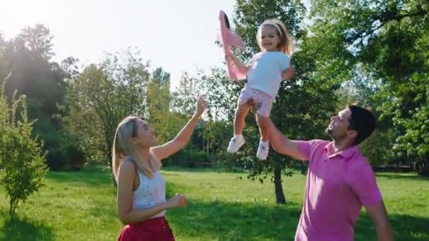 Großartige Eltern mit ihren Kindern haben eine lustige Zeit im Park auf dem Rasen beim Spielen mit dem Flugzeug und freuen sich, die Zeit zusammen zu verbringen — Stockvideo