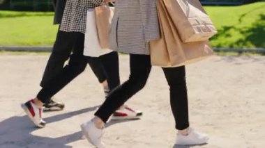 Kameraya yakın, modern sokak kadınlarından oluşan bir grupta yürüyorlar. Birlikte tartışıyorlar ve ellerinde alışveriş torbaları var.