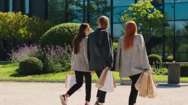 Frente a la cámara moderna edificio y grupo de mujeres jóvenes oficinas trabajadores caminando por la calle con algunas bolsas de compras — Vídeos de Stock