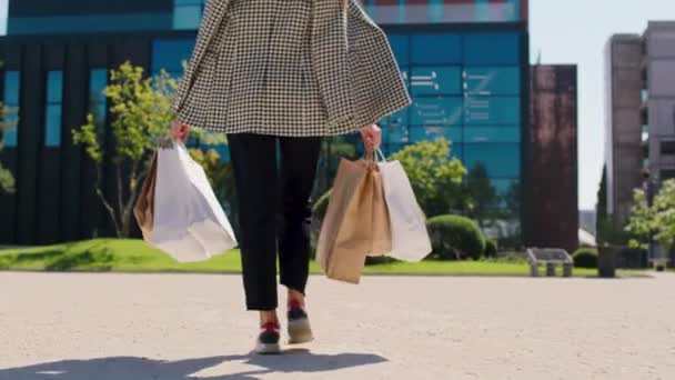 Mulher bonita andando lentamente depois de uma compra perfeita, ela segurando seus sacos de compras animado, ela desfrutar do sol ao lado de edifício arquitetônico moderno alto. 4k — Vídeo de Stock