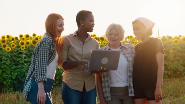 快乐而微笑的大个子漂亮的黑人女性与她的朋友和美丽的老祖母一起，用笔记本电脑记录了他们在相机前的向日葵的一些统计数据 — 图库视频影像