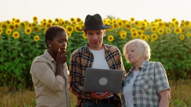 Charismatique fermier homme avec un grand sourire sa femme femme femme noire et sa mère ont une conversation au milieu du champ de tournesols ils discutent de leurs affaires ils sourient grand. Tourné sur ARRI — Video