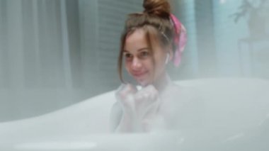 Genç bir kadın için dinlenme zamanı. Banyoda banyo yapar, akşamın tadını çıkarır ve kulaklıklardan müzik dinler.