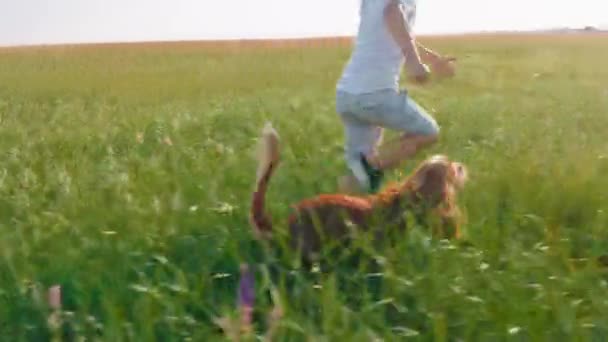 Framför kameran snygg hund och liten pojke som springer tillsammans genom det gröna fältet de njuta av ögonblicket tillsammans de är bästa vänner — Stockvideo