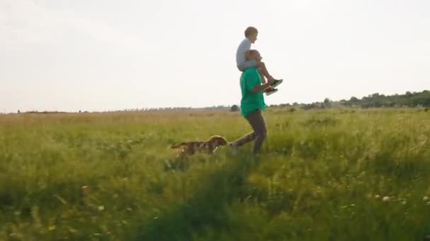 En la naturaleza corriendo hombre con una gran sonrisa junto con su lindo hijo pequeño en su espalda y después de ellos corriendo lindo perro pequeño Inglés cocker spaniel. Disparo en ARRI Alexa Mini. — Vídeos de Stock