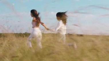 Güzel görünümlü iki genç kadın, doğanın ortasında yeşil alanda birlikte koşmaktan mutlular. Birlikte güzel bir an geçiriyorlar.