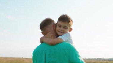 Karizmatik bir çocuğun portresi. Doğruca kameraya bakıyor. Yeşil tarlanın ortasında babasına sarılıyor.