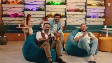 Üç iş arkadaşı fasulye koltuklarında otururken video oyunu oynuyorlar. Çok mutlu görünüyorlar ve eğleniyorlar.