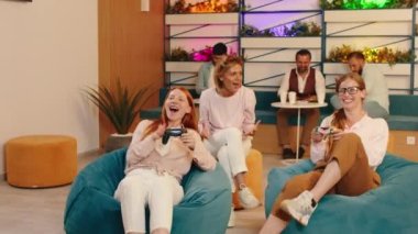 Üç güzel görünümlü kadın fasulye koltuklarında oturup video oyunları oynuyorlar.