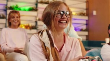 Çok rekabetçi sarışın bir kızın video oyununda kazandığı ve etrafındaki bir grup insanın da onun için mutlu olduğu için heyecanlandığı bir sahne.