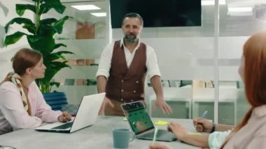 Gri sakallı ve saçlı çok yaşlı bir adam toplantıdaki takım üyeleriyle konuşuyor ve tartışıyor.