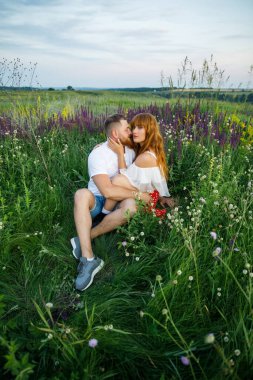 Pembe elbiseli, beyaz tişörtlü, beyaz tişörtlü, mavi şortlu genç ve güzel bir çift gün batımında çimlerin üzerinde eğleniyor.