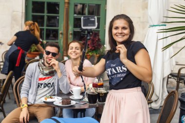 friends travelers sit at a table in a cafe in the old city of Europe at sunset and take a photo
