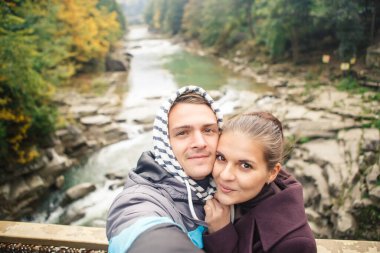 young beautiful couple travelers take a photo on the background of the river and forest