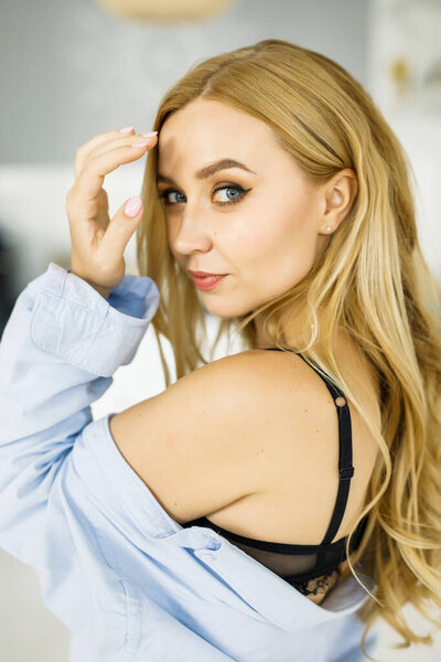 молодая красивая блондинка в голубой рубашке сидит у окна в светлой комнате