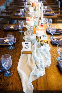 Şölen masası tabaklar, çatal bıçaklar, bardaklar, mumlar ve çiçek düzenlemeleri ile süslenir.