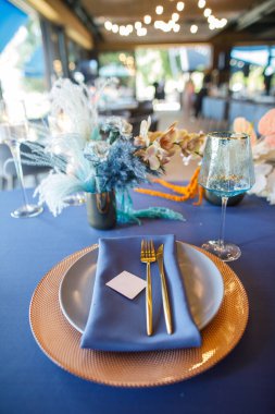 Şölen masası tabaklar, çatal bıçaklar, bardaklar, mumlar ve çiçek düzenlemeleri ile süslenir.