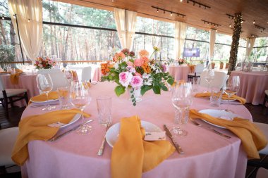 Şölen masası tabaklar, çatal bıçaklar, bardaklar, mumlar ve çiçek düzenlemeleri ile süslenir.