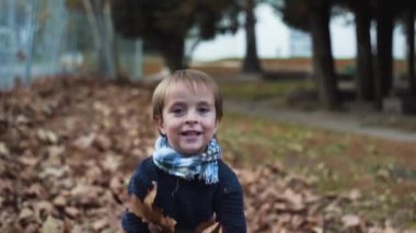 Sonbaharda yavaş çekimde yaprakları fırlatan çocuk.