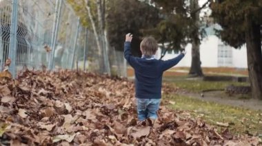 Neşeli küçük çocuk kuru sonbahar yapraklarında ağır çekimde koşuyor.