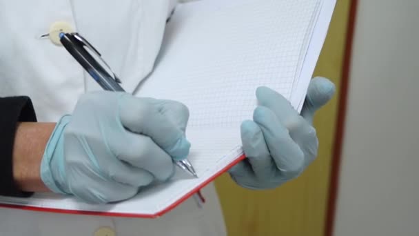 Médico en guantes de goma escribe en cuaderno — Vídeo de stock