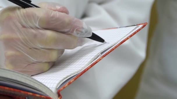 Médico en guantes de goma escribe en cuaderno — Vídeo de stock