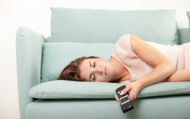 Young woman lying on couch and sleeping with TV remote control