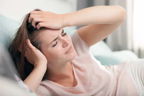 Young woman with headache lying on couch at home. Casual style indoor shoot — Stock Photo, Image