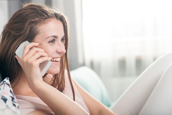Young woman sitting on couch at home and talking on mobile phone — Stock Photo, Image
