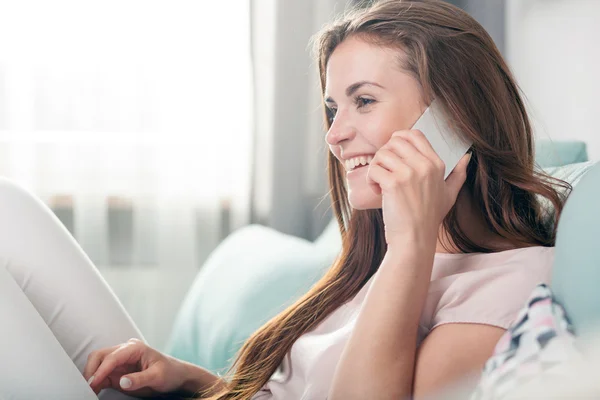 Mujer joven sentada en el sofá en casa y hablando por teléfono móvil —  Fotos de Stock