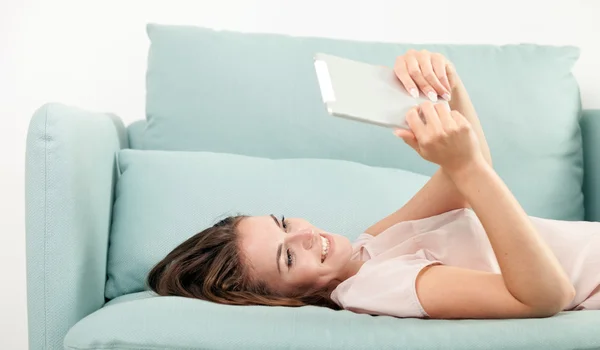 Jeune femme assise sur le canapé à la maison et la lecture ebook sur tablette. Style décontracté shoot intérieur — Photo