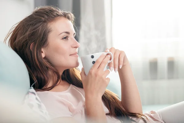 Mujer joven sentada en el sofá en casa y tomando café. Estilo casual sesión de interior — Foto de Stock