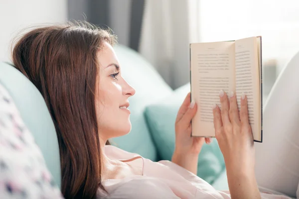 Young woman lying on couch and reading a book at home. Casual style indoor shoot — Stock Fotó