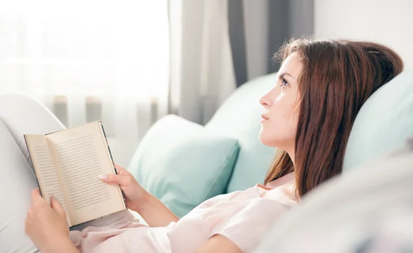Young woman lying on couch and reading a book at home. Casual style indoor shoot — Stock Fotó