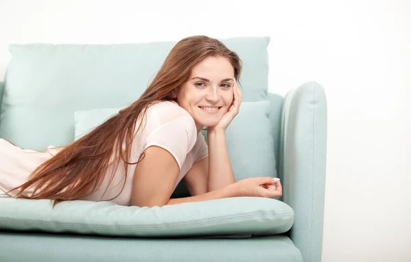 Giovane donna che ride e sdraiata sul divano a casa. Scatto in stile domestico — Foto Stock