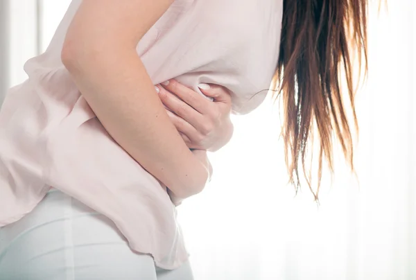 Young woman in pain holding her stomach. Casual style indoor shoot — Stok fotoğraf