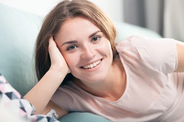 Happy young woman lying on couch at home and smiling. Casual style indoor shoot