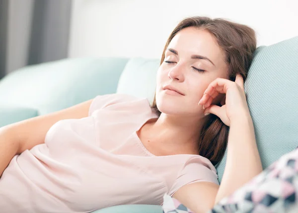 Wanita muda yang bahagia berbaring di sofa dan bersantai di rumah. Casual gaya menembak dalam ruangan — Stok Foto