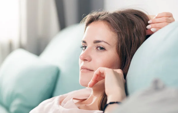 Wanita muda yang bahagia berbaring di sofa dan bersantai di rumah. Casual gaya menembak dalam ruangan — Stok Foto