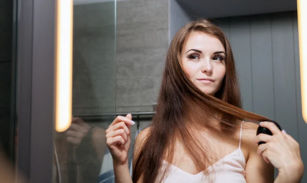 Kobieta, szczotkowanie włosów przed lustrem łazienka — Zdjęcie stockowe