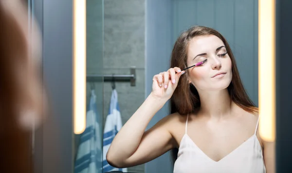 Woman applying mascara on long eyelashes in front of mirror — Stock Photo, Image