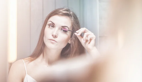 Frau trägt Wimperntusche auf langen Wimpern vor Spiegel auf — Stockfoto