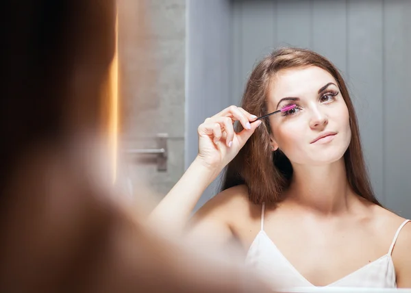 Frau trägt Wimperntusche auf langen Wimpern vor Spiegel auf — Stockfoto