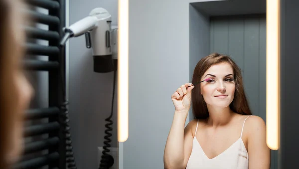 Frau trägt Wimperntusche auf langen Wimpern vor Spiegel auf — Stockfoto