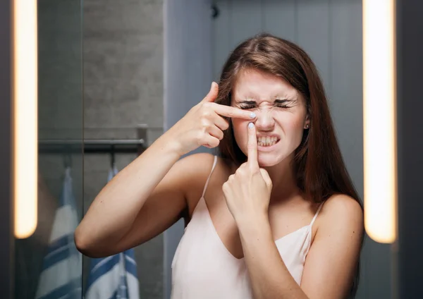 Mujer apretando espinillas delante de un espejo de baño —  Fotos de Stock