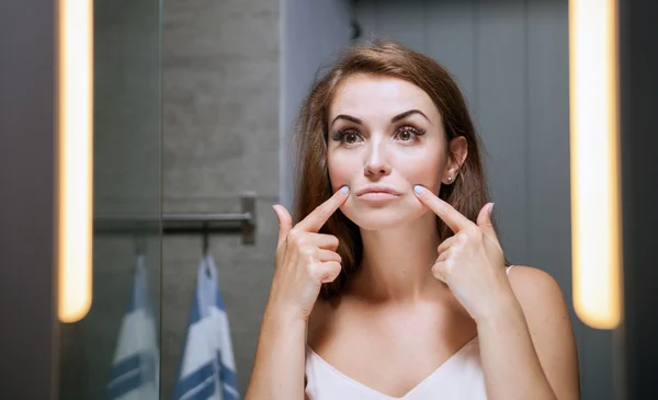 Woman checking wrinkles on face in front of bathroom mirror — Stock Photo, Image