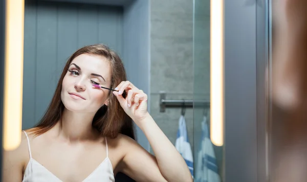 Frau trägt Wimperntusche auf langen Wimpern vor Spiegel auf — Stockfoto